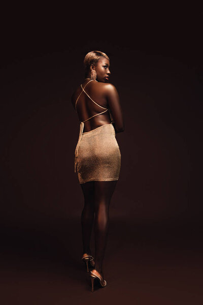 beautiful elegant african american woman with short hair posing in glamorous dress on brown