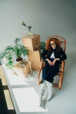 Ahşap kutular, gözlük ve bitkiler yakın hasır sandalyede şık Redhead kız yüksek açı görünümü