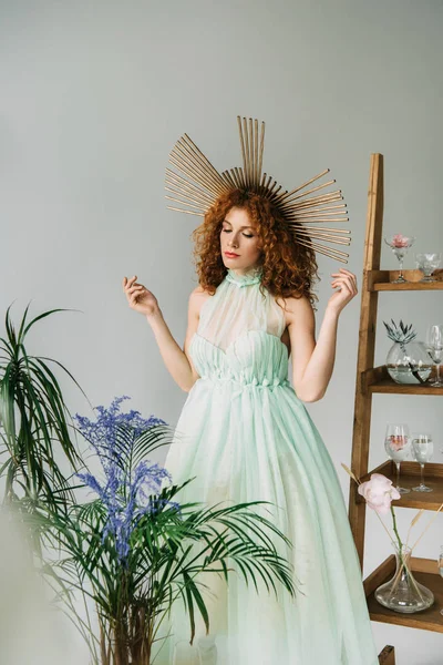 redhead girl with accessory on head in dress posing near plants and ladder