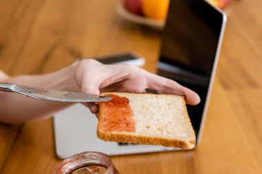 Masanın yanında elinde bıçak ve tost ve reçel olan bir kadın görüntüsü. 