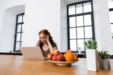 Heyecanlı serbest yazar masasında aletlerin, meyvelerin ve bitkilerin yanında oturuyor. 