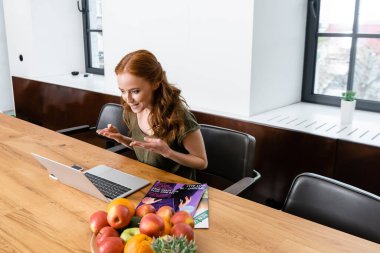 Gülümseyen serbest çalışanın seçmeli odak noktası elleri ile işaret ederken evdeki bilgisayarda görüntülü arama 