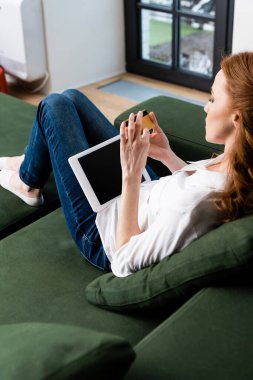 Selective focus of woman holding credit cad and digital tablet on couch at home  clipart