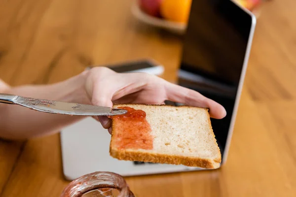 Cropped View Woman Holding Knife Toast Jam Laptop Table — Stock Photo, Image