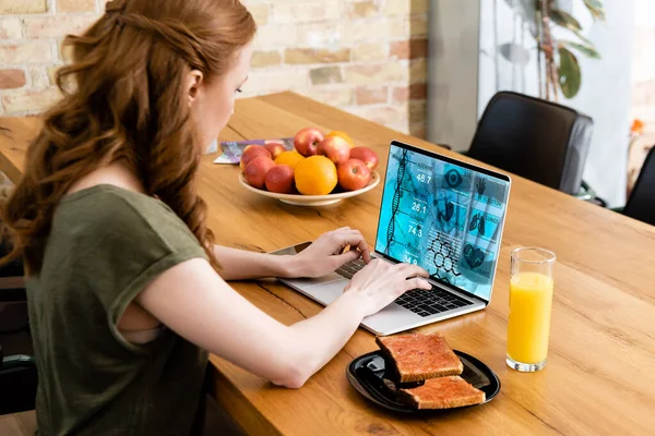 在木制桌子上的橙汁和烘培杯旁边 女性使用带有E Health网站的笔记本电脑的侧视图 — 图库照片