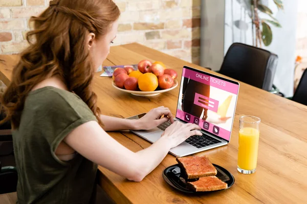 女性在烤面包和橙汁桌旁在线售票网站使用笔记本电脑的侧视图 — 图库照片