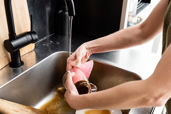 Cropped view of woman cleaning cup with rag in kitchen sink 