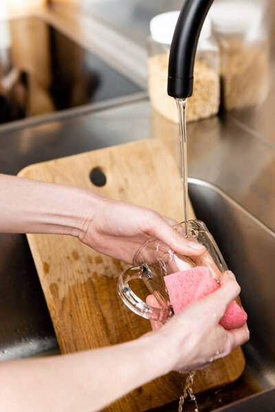 Cropped view of woman cleaning cup near chopping board in kitchen sink 