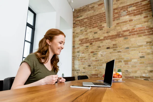 Uśmiechnięta Freelancer Patrząc Laptopa Pobliżu Smartfona Stole — Zdjęcie stockowe