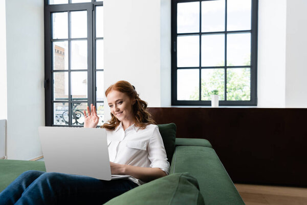 Selective focus of smiling woman having video call on laptop at home 