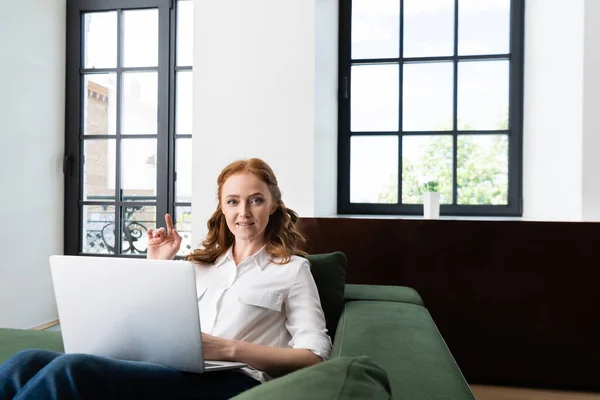 自宅でソファの上にラップトップを使用している間に指で指す女性の選択的な焦点 — ストック写真