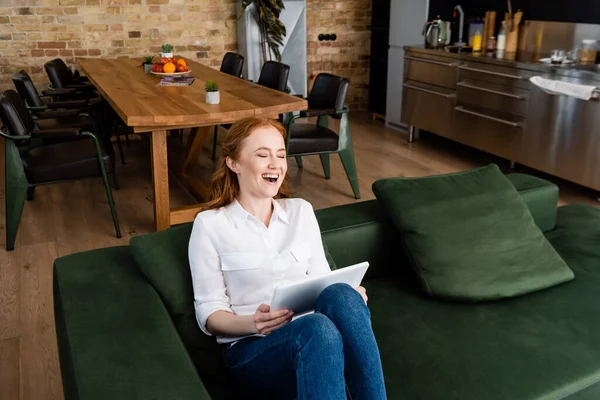 自宅でソファの上でデジタルタブレットを使用している間に笑う魅力的な女性 — ストック写真