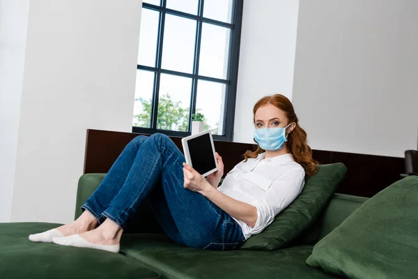 女性で医療用マスクショーデジタルタブレットとともにブランクスクリーンオンソファ — ストック写真