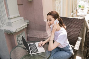 Neşeli serbest çalışan masadaki bilgisayarın yanında akıllı telefondan konuşuyor.