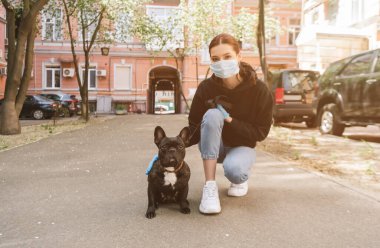 Tıbbi maskeli ve lateks eldivenli bir kadın caddede tatlı bir Fransız bulldog 'una dokunuyor. 