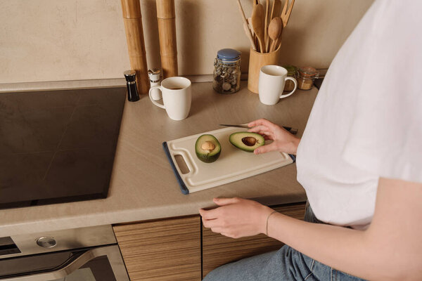 cropped view of woman touching half of tasty avocado near cups 