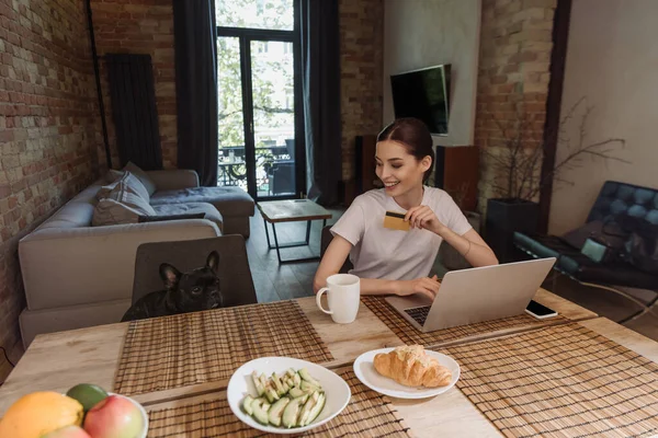 Szczęśliwy Młoda Kobieta Trzyma Kartę Kredytową Pobliżu Laptopa Patrząc Francuski — Zdjęcie stockowe