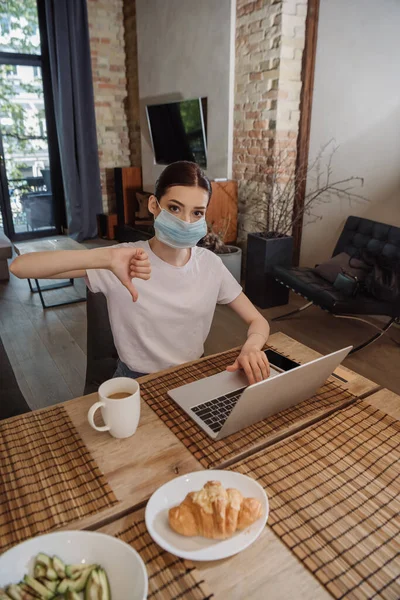 Jovem Freelancer Máscara Médica Mostrando Polegar Para Baixo Perto Laptop — Fotografia de Stock