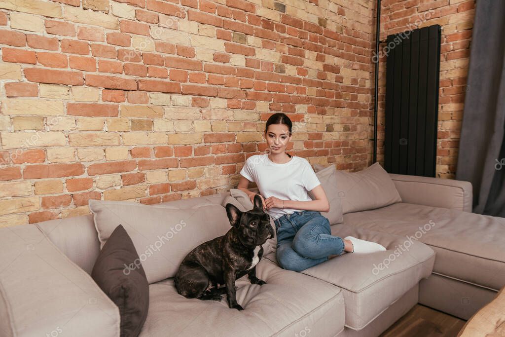 Cute french bulldog and attractive girl sitting on sofa in living room