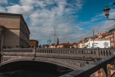 COPENHAGEN, DENMARK - 30 Nisan 2020: Köprüde binalar ve arka planda bulutlu gökyüzü ile yürüyen insanlar 