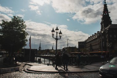 COPENHAGEN, DENMARK - 30 Nisan 2020: Kentsel caddede Christiansborg Sarayı ve bulutlu gökyüzü olan insanlar 