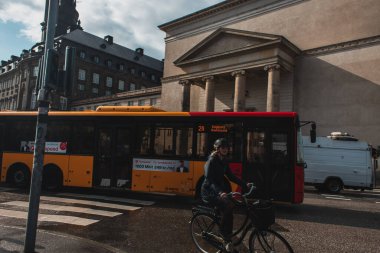 COPENHAGEN, DENMARK - 30 Nisan 2020: Otobüslerin yanında bisiklet süren kadın  