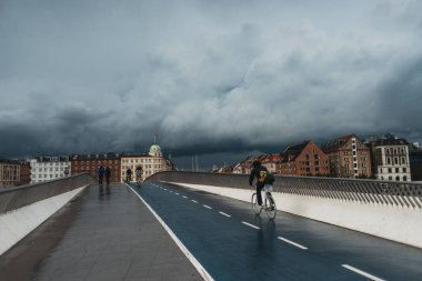 COPENHAGEN, DENMARK - 30 Nisan 2020: Köprüde şehir caddesi ve arka planda bulutlu gökyüzü ile yürüyen insanlar 