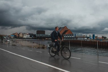 COPENHAGEN, DENMARK - 30 Nisan 2020: Arka planda bulutlu gökyüzü olan şehir caddesinde bisiklet süren adam 