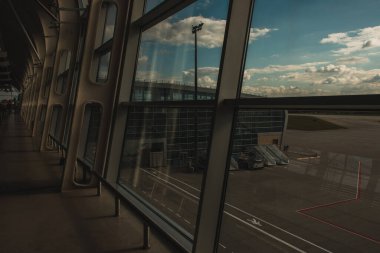 Arka planda bulutlu gökyüzü olan havaalanı binasının ön cephesi olan pencere camı 