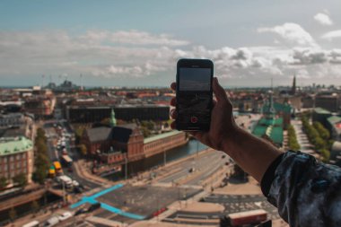 Cropped view of tourist taking picture on smartphone with Copenhagen city at background, Denmark  clipart