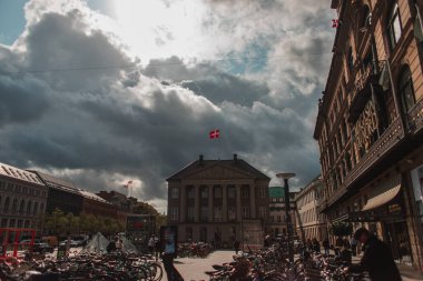 COPENHAGEN, DENMARK - 30 Nisan 2020: Arkaplanda binalar ve bulutlu gökyüzü olan şehir meydanında bisikletler 