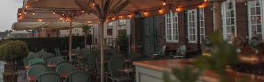 Panoramic crop of lighting on umbrellas of near tables and chairs of outdoor cafe in Copenhagen, Denmark  clipart