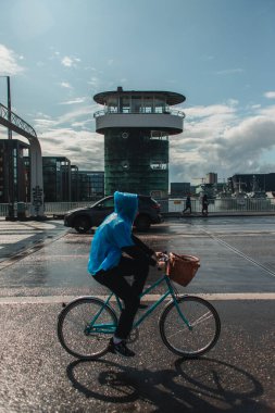 COPENHAGEN, DENMARK - 30 Nisan 2020: Yağmurdan sonra şehir caddesinde bisiklet süren kadının yan görünümü 