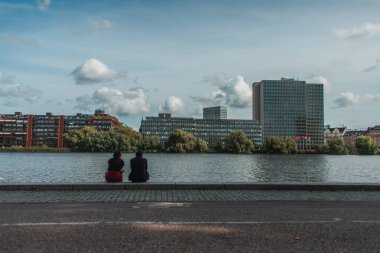İnsanlar kanal kenarında oturuyorlar, binalar ve arka planda bulutlu gökyüzü, Kopenhag, Danimarka 