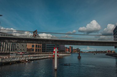 COPENHAGEN, DENMARK - 30 Nisan 2020: Nehrin yukarısında şehir caddesi ve gökyüzü bulutlu köprüde bisiklet süren insanlar 