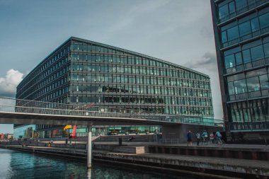 COPENHAGEN, DENMARK - 30 Nisan 2020: Köprü yakınındaki bisikletli insanlar ve arka plandaki kentsel caddedeki binalar