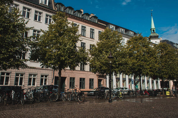 COPENHAGEN, DENMARK - APRIL 30, 2020: Bicycles near trees on urban street with buildings and blue sky at background 