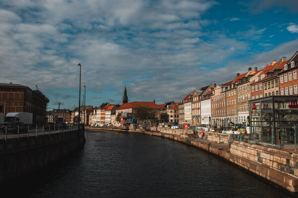COPENHAGEN, DENMARK - APRIL 30, 2020: Canal with buildings on promenade and cloudy sky at background