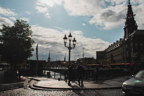 COPENHAGEN, DENMARK - APRIL 30, 2020: People on urban street with Christiansborg Palace and cloudy sky at background 
