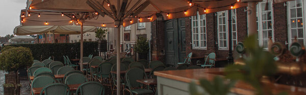 Panoramic crop of lighting on umbrellas of near tables and chairs of outdoor cafe in Copenhagen, Denmark 