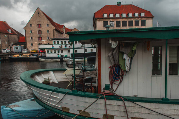 Docked boats in harbor with buildings and cloudy sky at background in Copenhagen, Denmark 