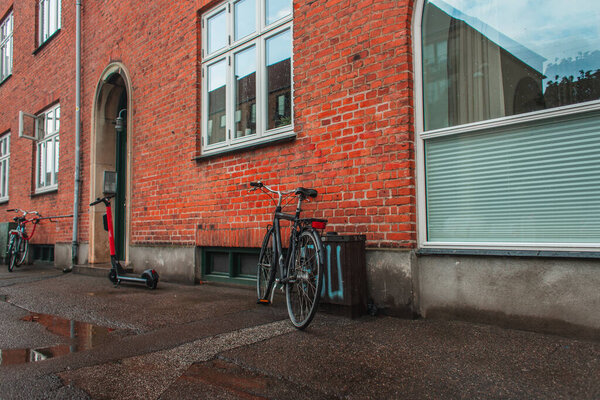 Bikes and scooter near brick facade of building on urban street in Copenhagen, Denmark 