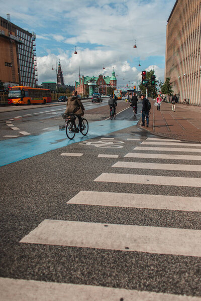 COPENHAGEN, DENMARK - APRIL 30, 2020: People walking and cycling on urban street with cloudy sky at background 