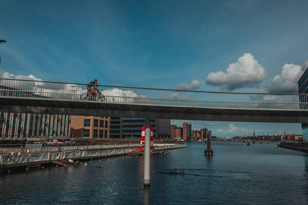 COPENHAGEN, DENMARK - APRIL 30, 2020: People cycling on bridge above river with urban street and sky with clouds at background 