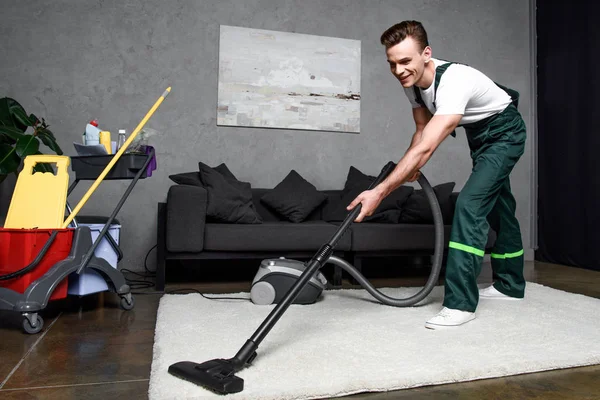 Smiling young professional cleaner cleaning carpet with vacuum cleaner — Stock Photo