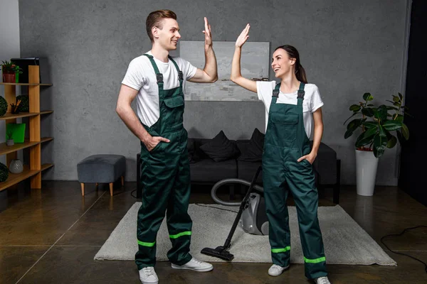 Glückliche junge professionelle Reinigungskräfte lächeln einander zu und geben High Five — Stockfoto