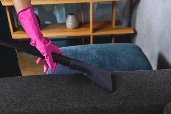 Partial view of person in rubber glove cleaning furniture with vacuum cleaner — Stock Photo