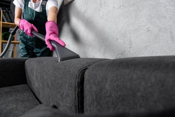 Cropped shot of woman in rubber gloves cleaning sofa with vacuum cleaner — Stock Photo