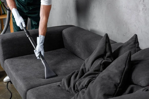 Обрезанный снимок человека в резиновых перчатках с помощью пылесоса и чистящего дивана — стоковое фото