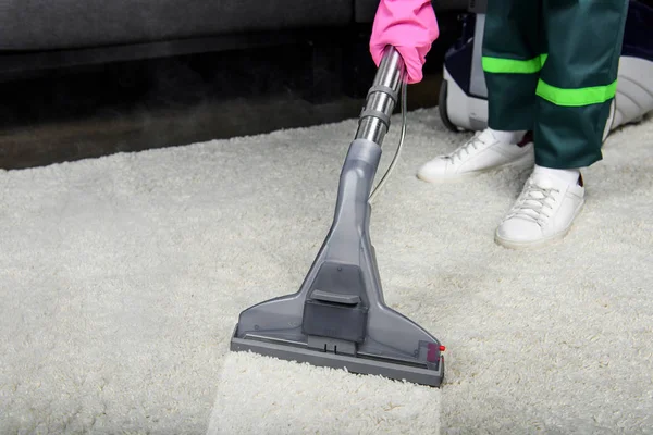 Tiro recortado de la persona en la alfombra de limpieza de guantes de goma con aspiradora - foto de stock